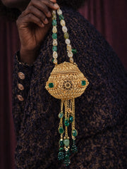 Person holding a gold orb potli bag with emerald accents and beaded handle, wearing a patterned garment