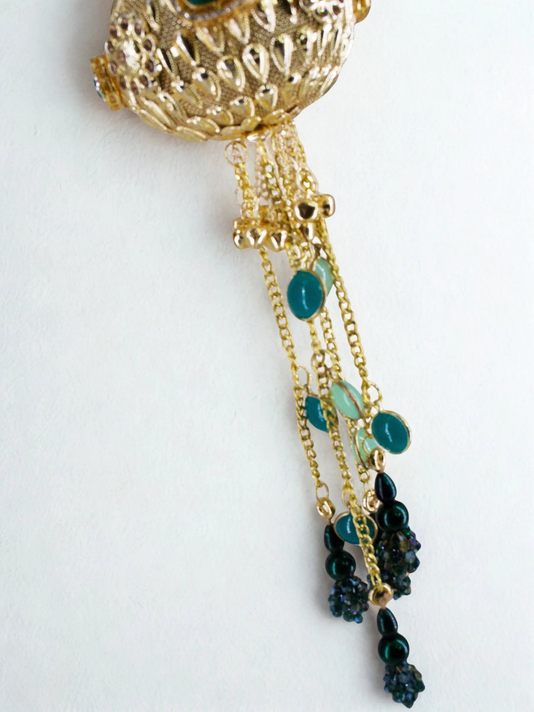 Close-up of gold orb potli bag showing beaded chain tassels with green and black stone droplets on a white background