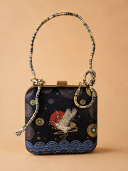 Midnight Crane Clutch, a square box clutch in navy fabric embroidered with a flying crane over a red sun, gold circular motifs, and a wave border, with a snake-shaped metallic top handle.