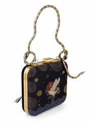 Angled view of the Midnight Crane Clutch showing the snake-shaped metallic handle and the embroidered crane and wave motif on the navy front panel.