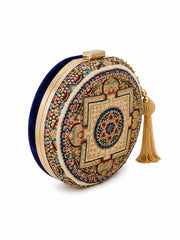 An ornate round clutch bag featuring a gold-tone metal frame, a navy blue velvet side, and an intricate multicolor embroidered central mandala design with a gold tassel.