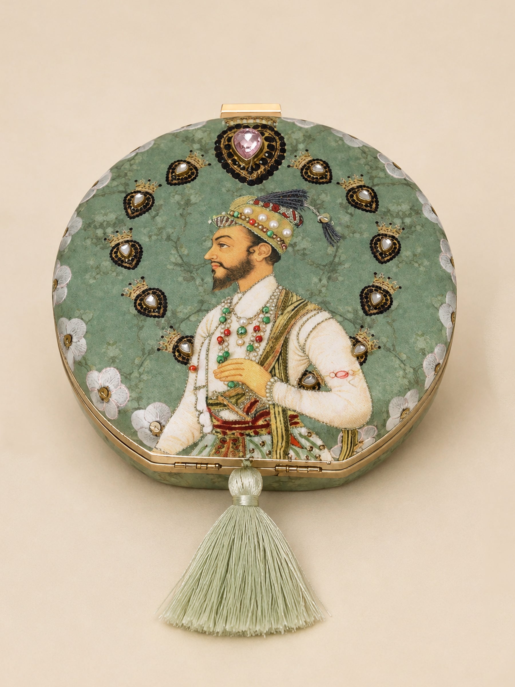 Raazdaar Embroidered Clutch, a round clutch in sage green fabric with a Mughal-style miniature portrait of a nobleman, a jeweled heart-shaped medallion, and a silk tassel.