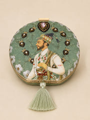 Raazdaar Embroidered Clutch, a round clutch in sage green fabric with a Mughal-style miniature portrait of a nobleman, a jeweled heart-shaped medallion, and a silk tassel.
