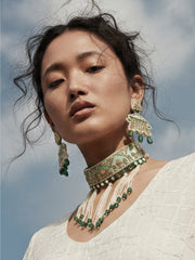 Woman wearing elaborate green and gold jewelry against a blue sky.