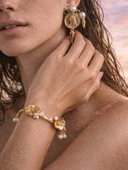 Close-up of a woman wearing gold earrings and bracelet against a blurred natural background