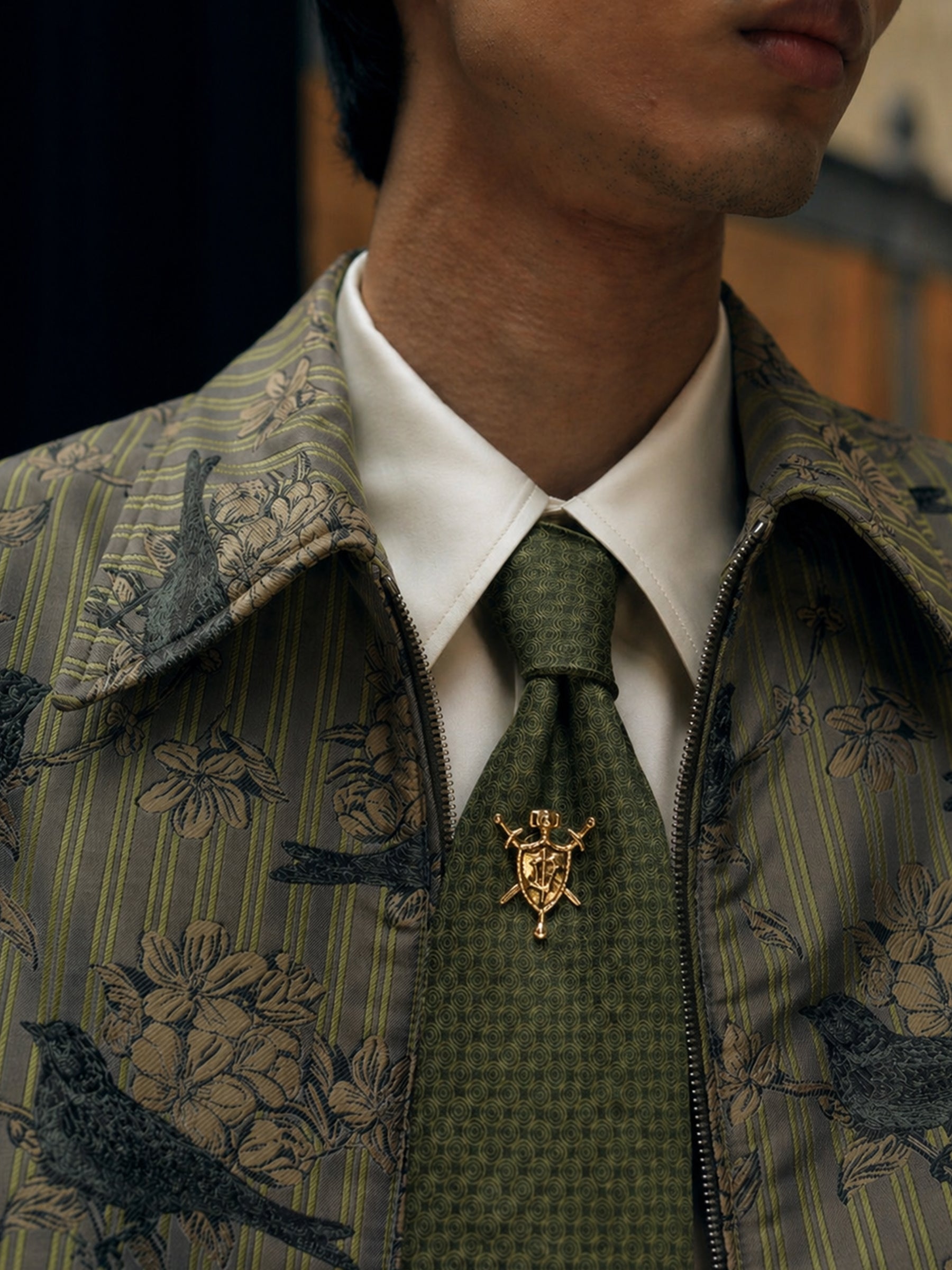 Man wearing a patterned jacket with a white shirt and green tie, close-up of neck and chest area.