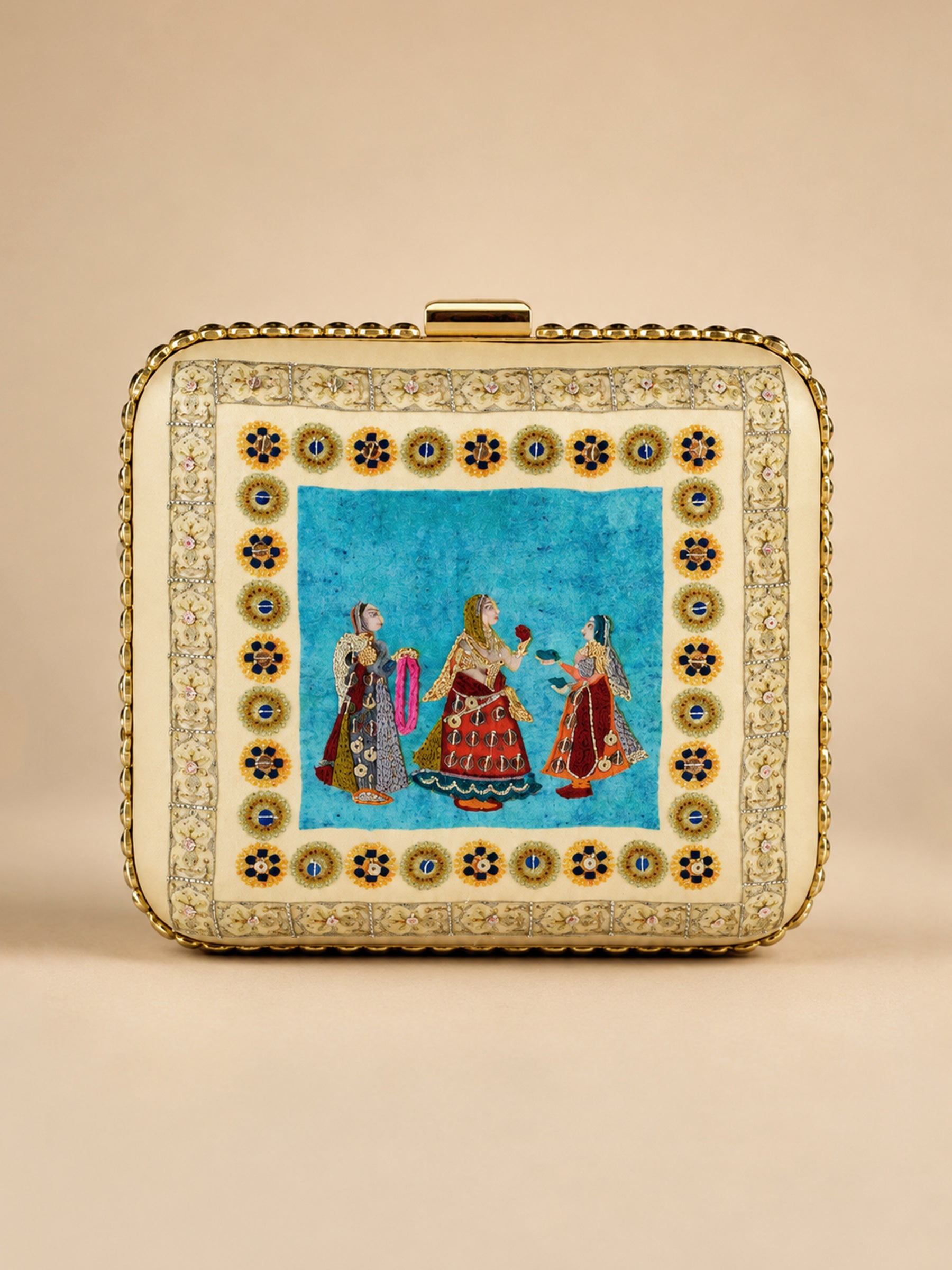 Saheliya Embroidered Clutch, a square box clutch in cream and turquoise velvet with a hand-embroidered panel depicting three traditional Rajasthani women in colorful attire, framed by a gold floral medallion border and a gold clasp.